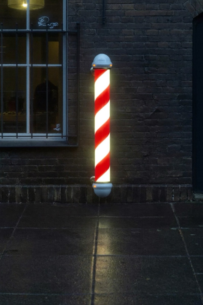 Glowing barber pole against a brick wall at dusk